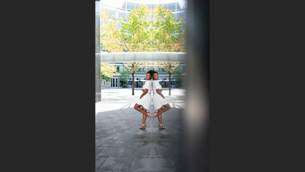 Black woman leans on a mirror wall next to tree